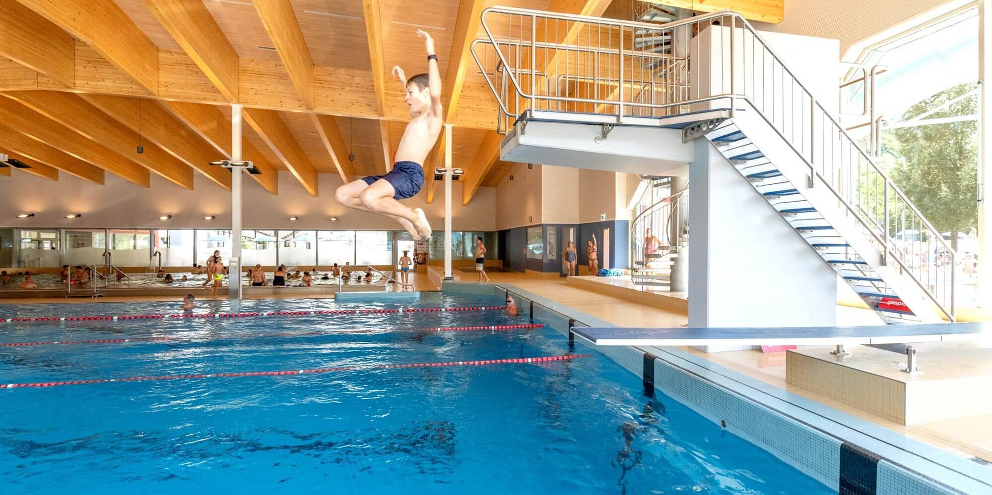 Junge springt von Sprungturm ins Hallenbadbecken