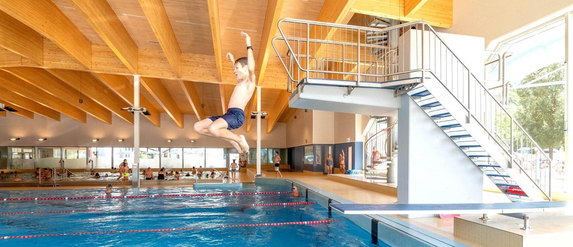 Junge springt von Sprungturm ins Hallenbadbecken
