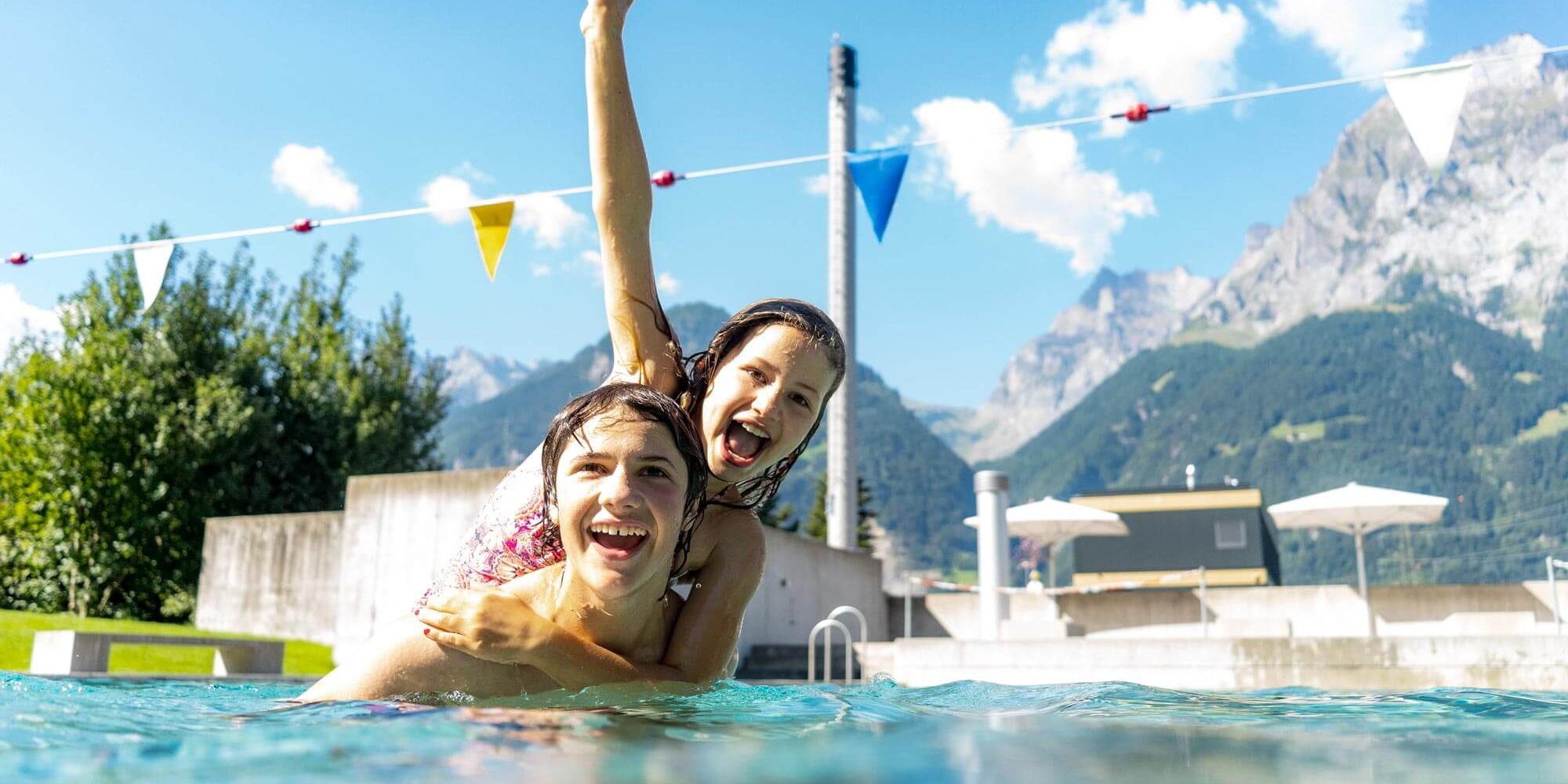 Kinder spielen im Freibad mit Bergpanorama